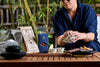 Person preparing tea at a wooden table with tea packaging and snacks.